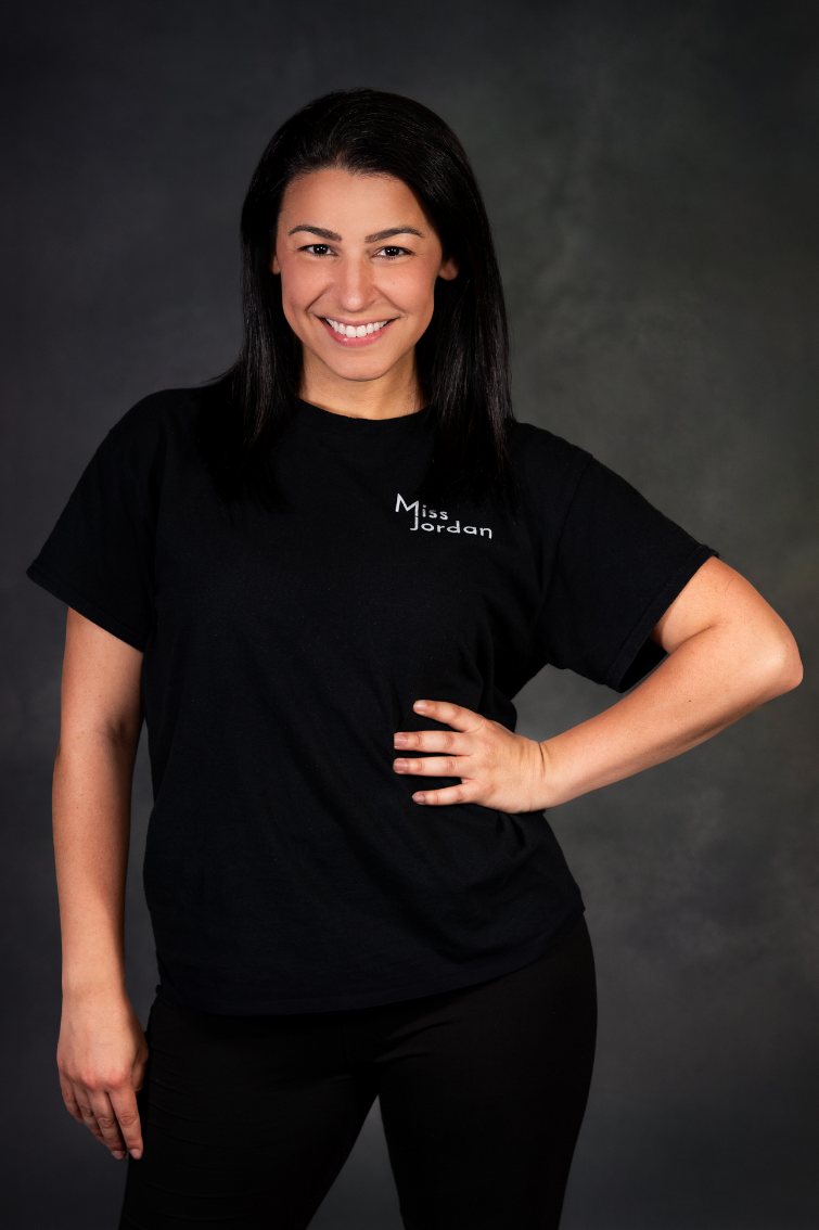 Jordan Rodrigues, owner of Empowered Movement, smiling and wearing her black Miss Jordan studio shirt