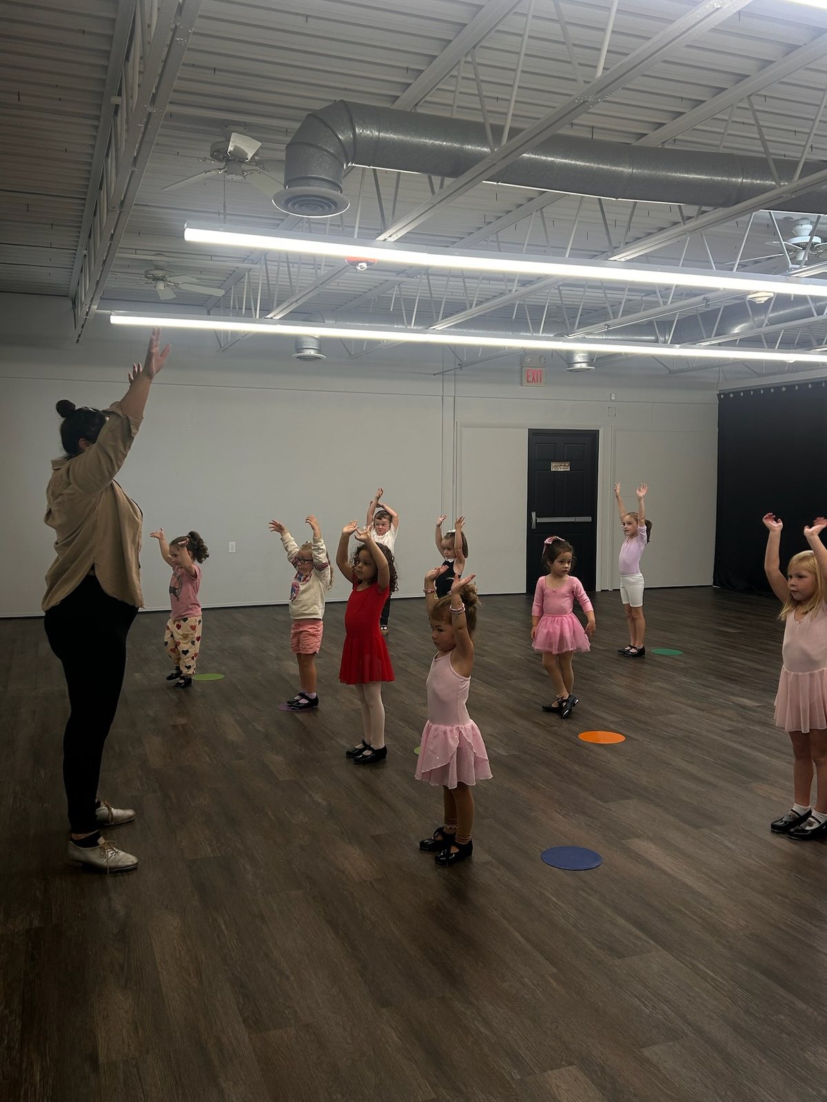 A teacher leading a creative movement class as young children raise their arms